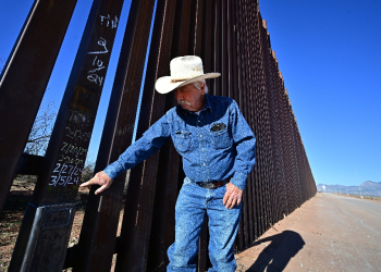 Cattle rancher John Ladd points to dates written on a lower section of the thirty-foot tall US-Mexico border wall marking repairs made after the wall was compromised by migrants crossing into his land from Mexico / ©AFP