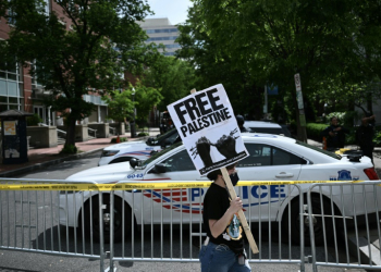 A demonstrator holds a sign as a police vehicle and barricades block a road after officers cleared a pro-Palestinian student protest encampment at George Washington University on May 8, 2024. ©AFP
